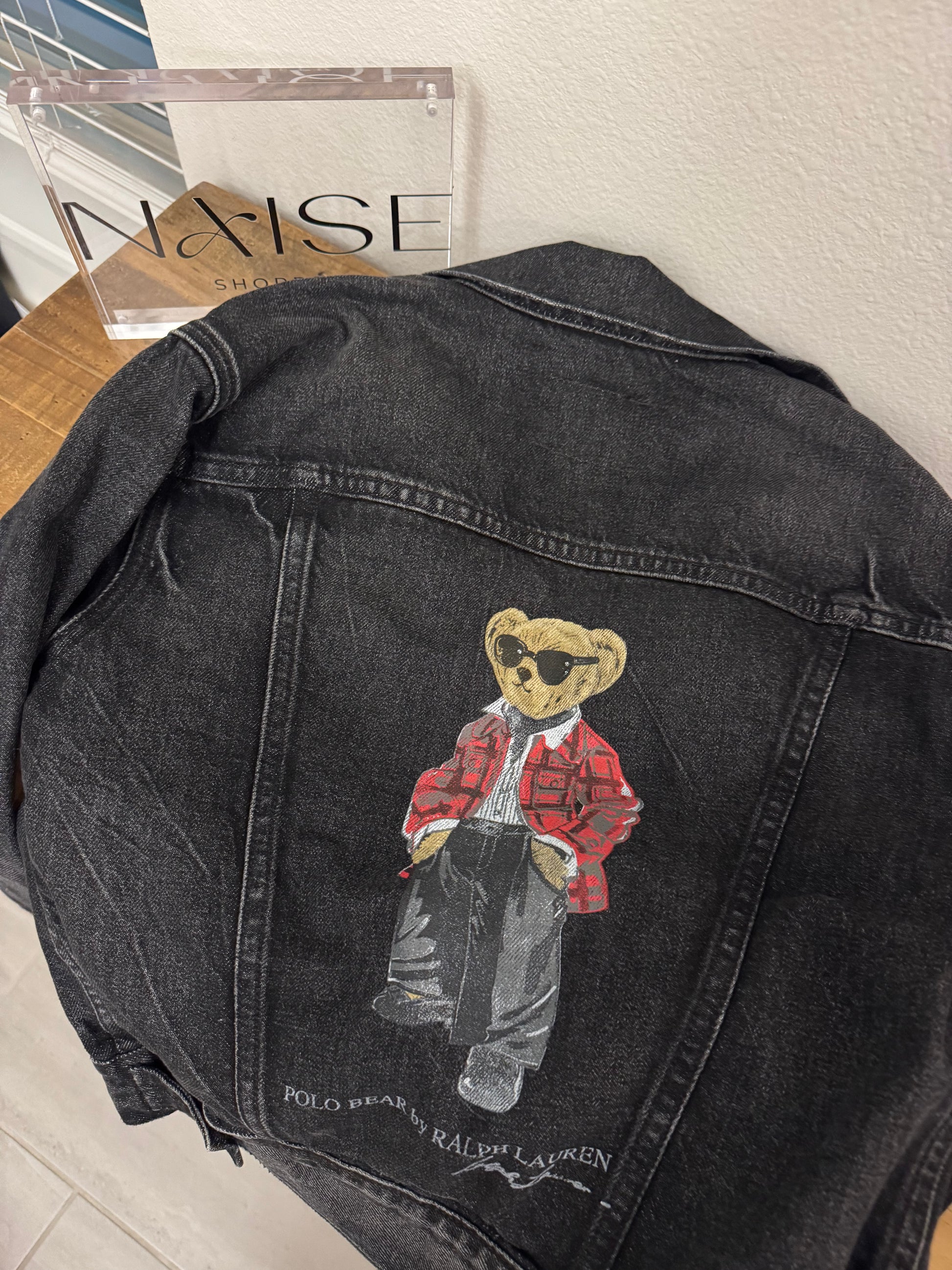Black denim jacket with a bear graphic on a wooden surface
