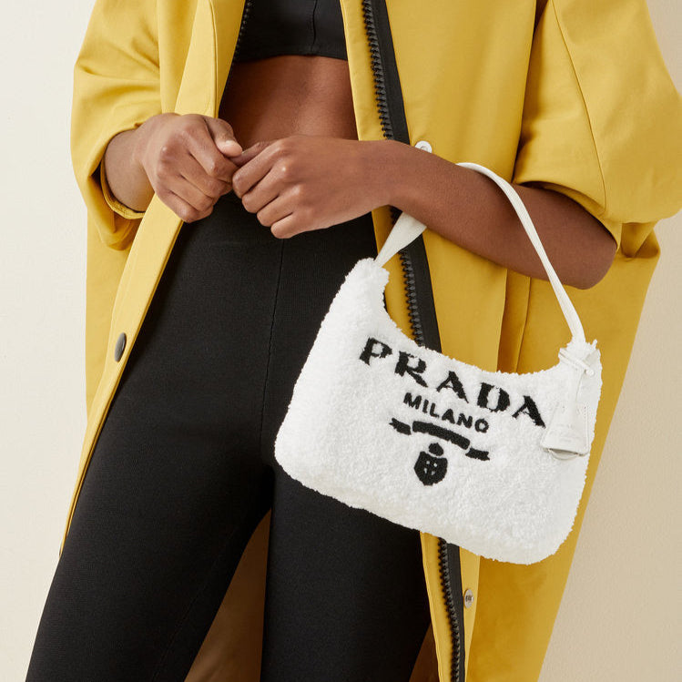 Person wearing a yellow raincoat holding a white Prada bag against a neutral background