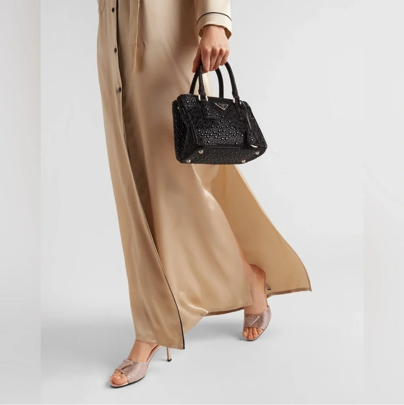 Person holding a black handbag wearing a beige dress on a white background