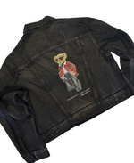 Black denim jacket with embroidered bear design on a beige surface