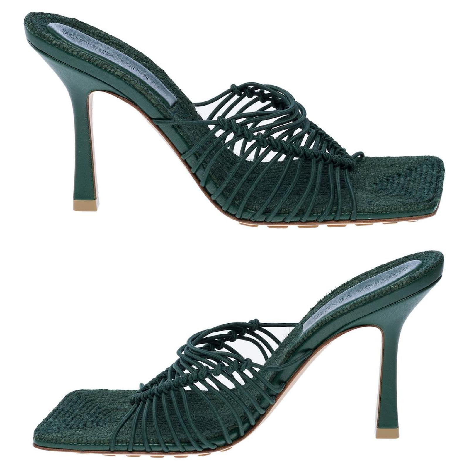 Pair of green high-heeled shoes with woven design on a white background