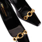 Black high-heeled shoes with gold chain details and 'Saint Laurent' branding on a light gray background.