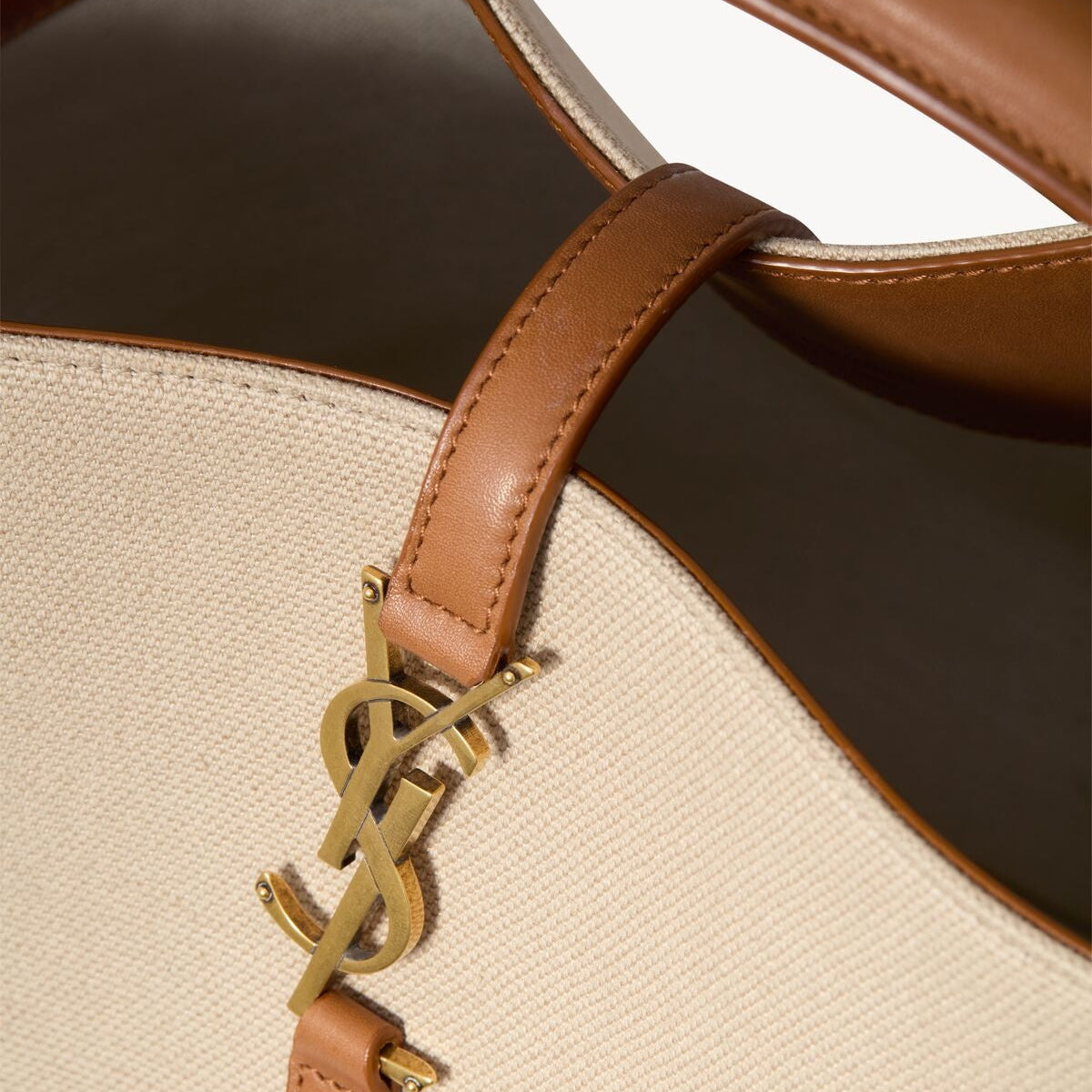 Close-up of a beige handbag with brown leather handle and YSL logo.