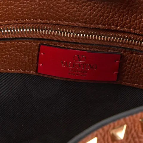 Close-up of a brown leather bag with a red label featuring a brand logo.