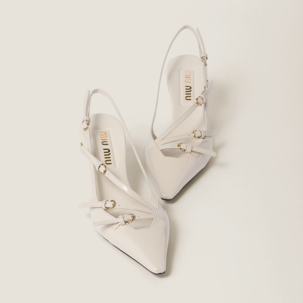 White pointed-toe slingback shoes with 'Miu Miu' branding on a light gray background