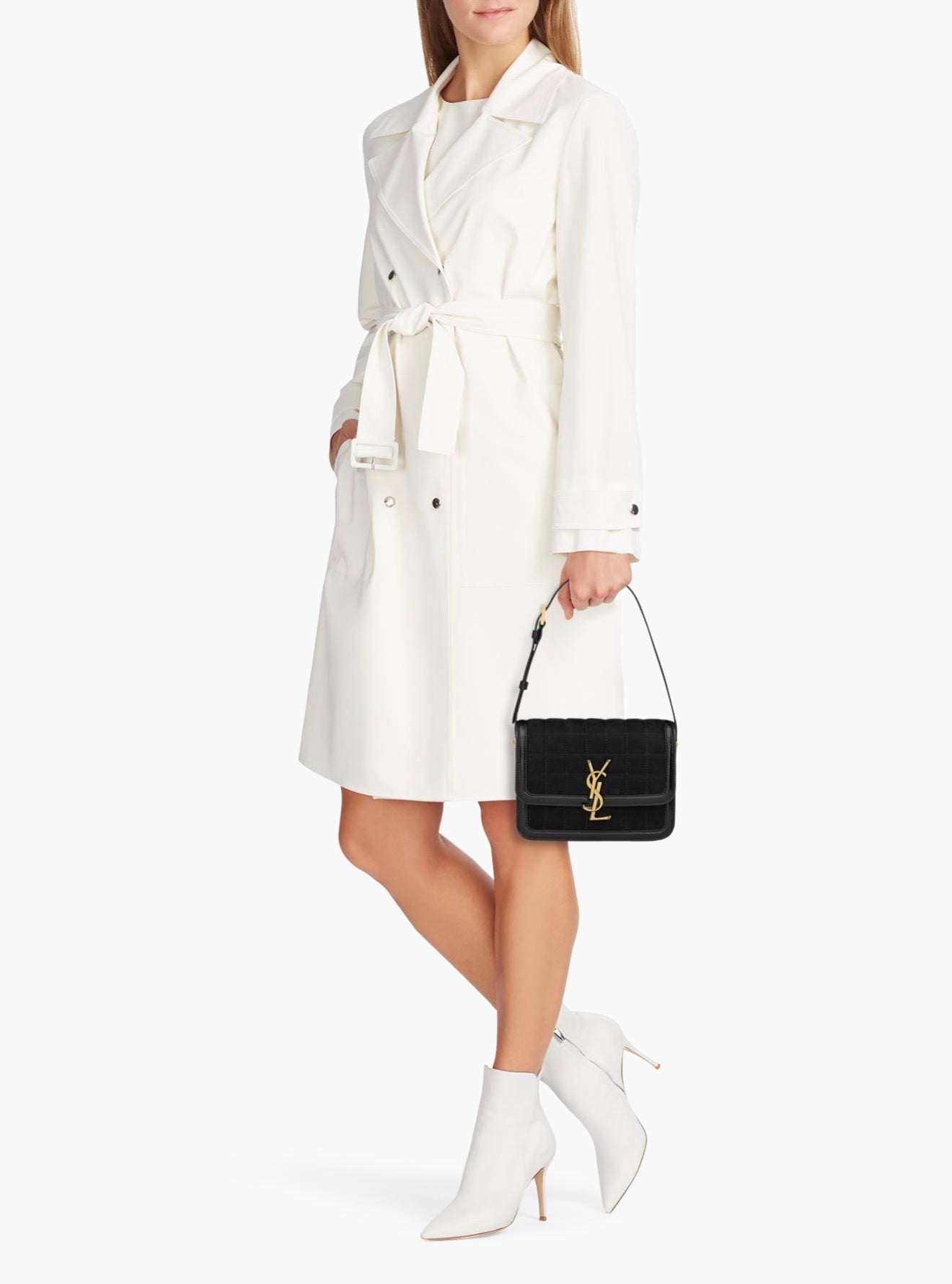 Person wearing a white trench coat holding a black handbag with a brand logo on a white background