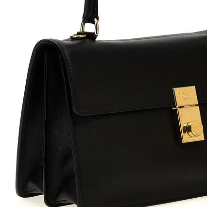 A close-up of a black leather handbag with a gold-tone turn-lock clasp and a gold brand plaque on the front flap, set against a plain white background.