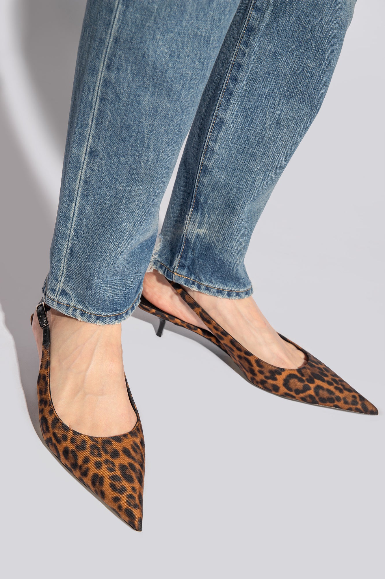 Leopard print shoes worn with blue jeans on a light gray background