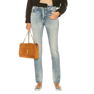 Woman wearing a black jacket, beige top, and blue jeans, holding a brown handbag on a white background