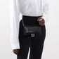 Person wearing a white shirt and black pants holding a black sequin handbag.