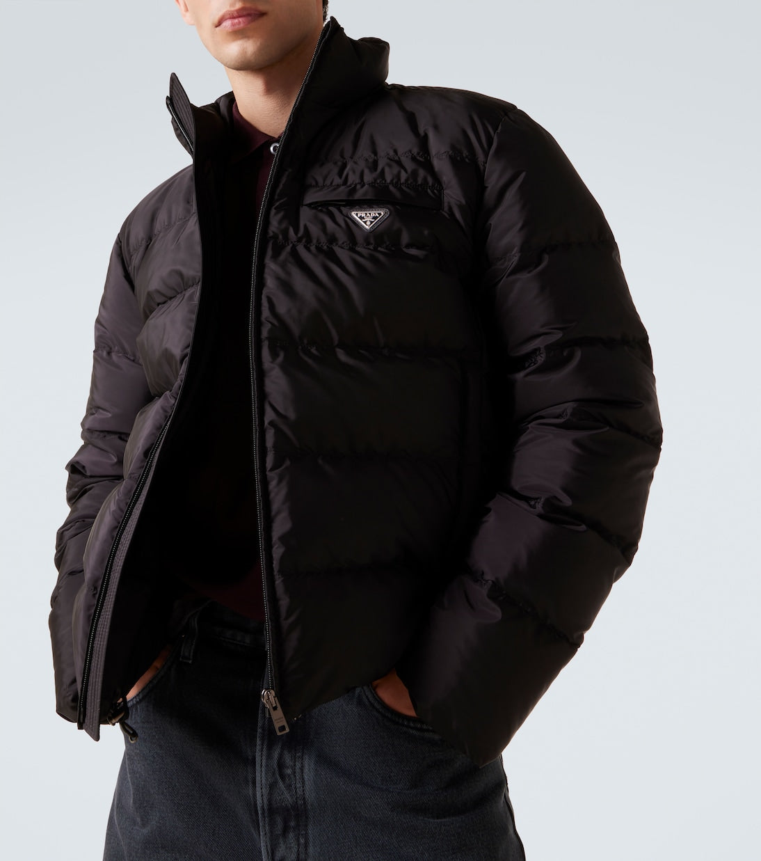 Person wearing a black puffer jacket with a brand logo on a light gray background