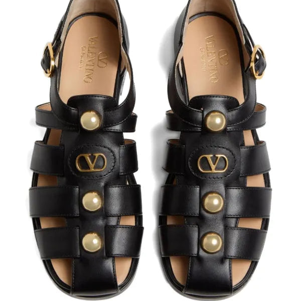 Black sandals with pearl embellishments and gold logo on a white background