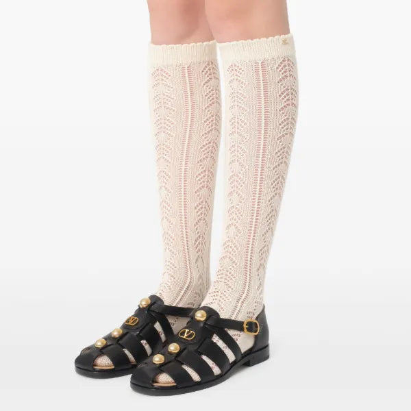 White knee-high knitted socks worn with black sandals on a white background