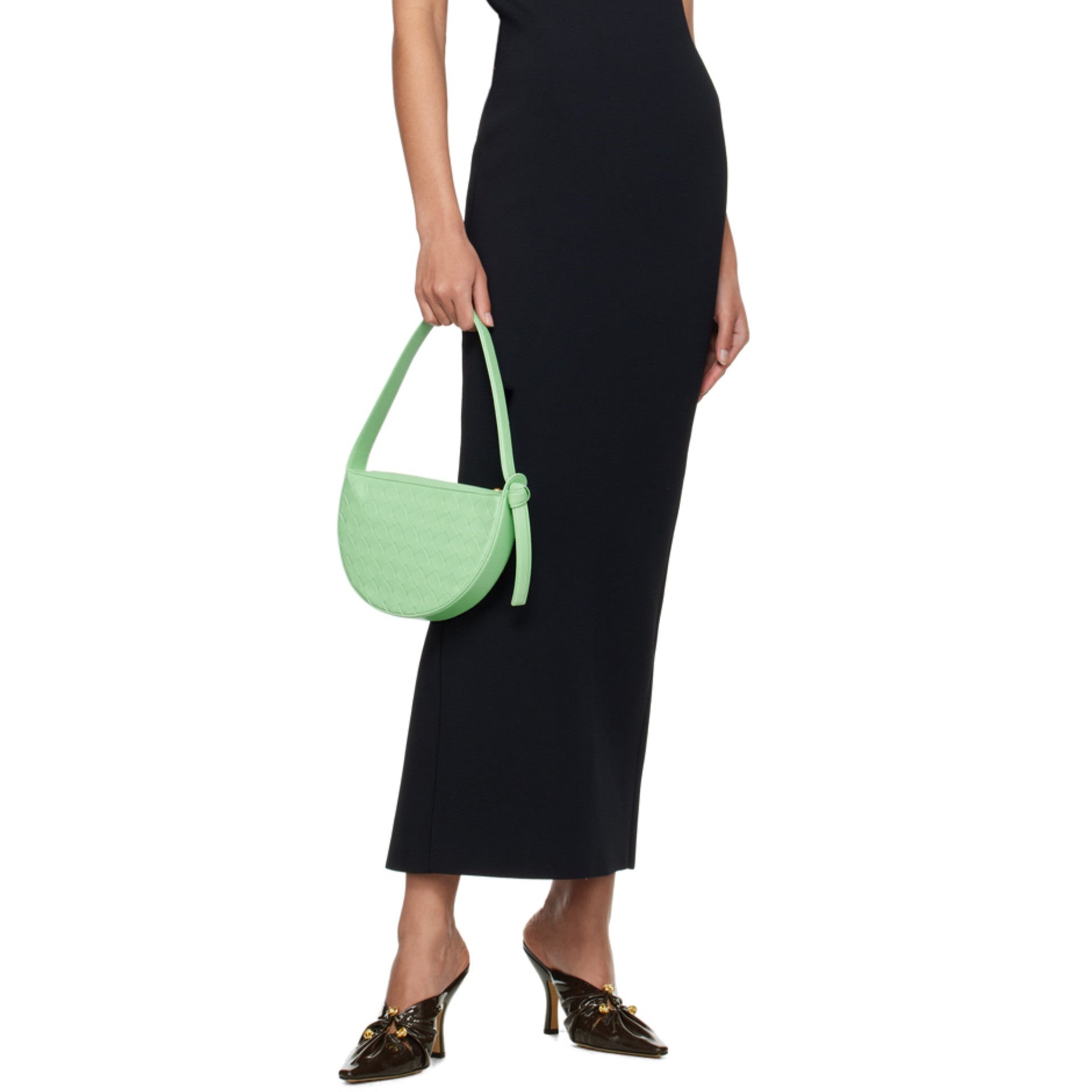 Woman wearing a black strapless dress holding a green luxury Bottega handbag on a white background