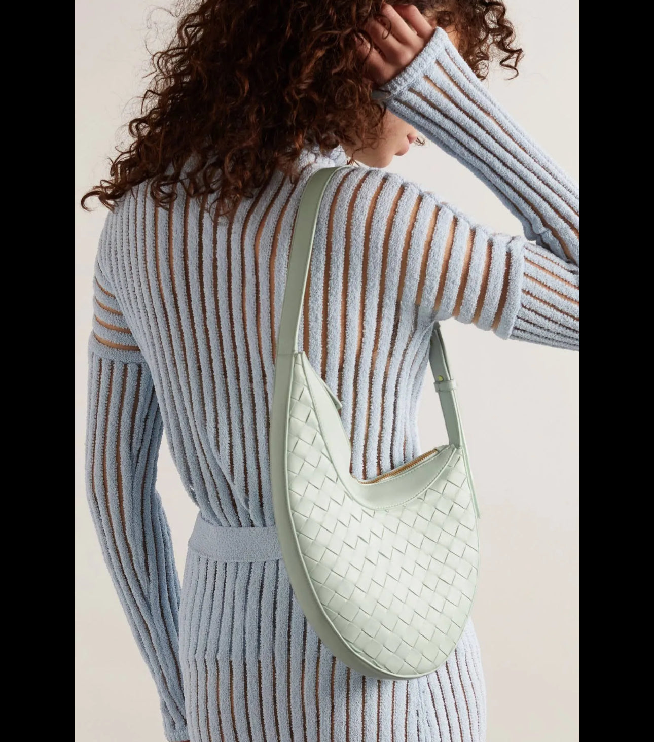 Person wearing a light gray ribbed sweater and holding a light green woven handbag.