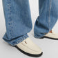 White loafers with a brand logo worn with blue jeans on a light gray background