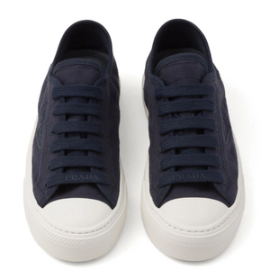 Pair of navy blue luxury Prada sneakers with white soles on a white background