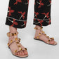 Pink studded sandals worn with black pants featuring red floral patterns on a white background