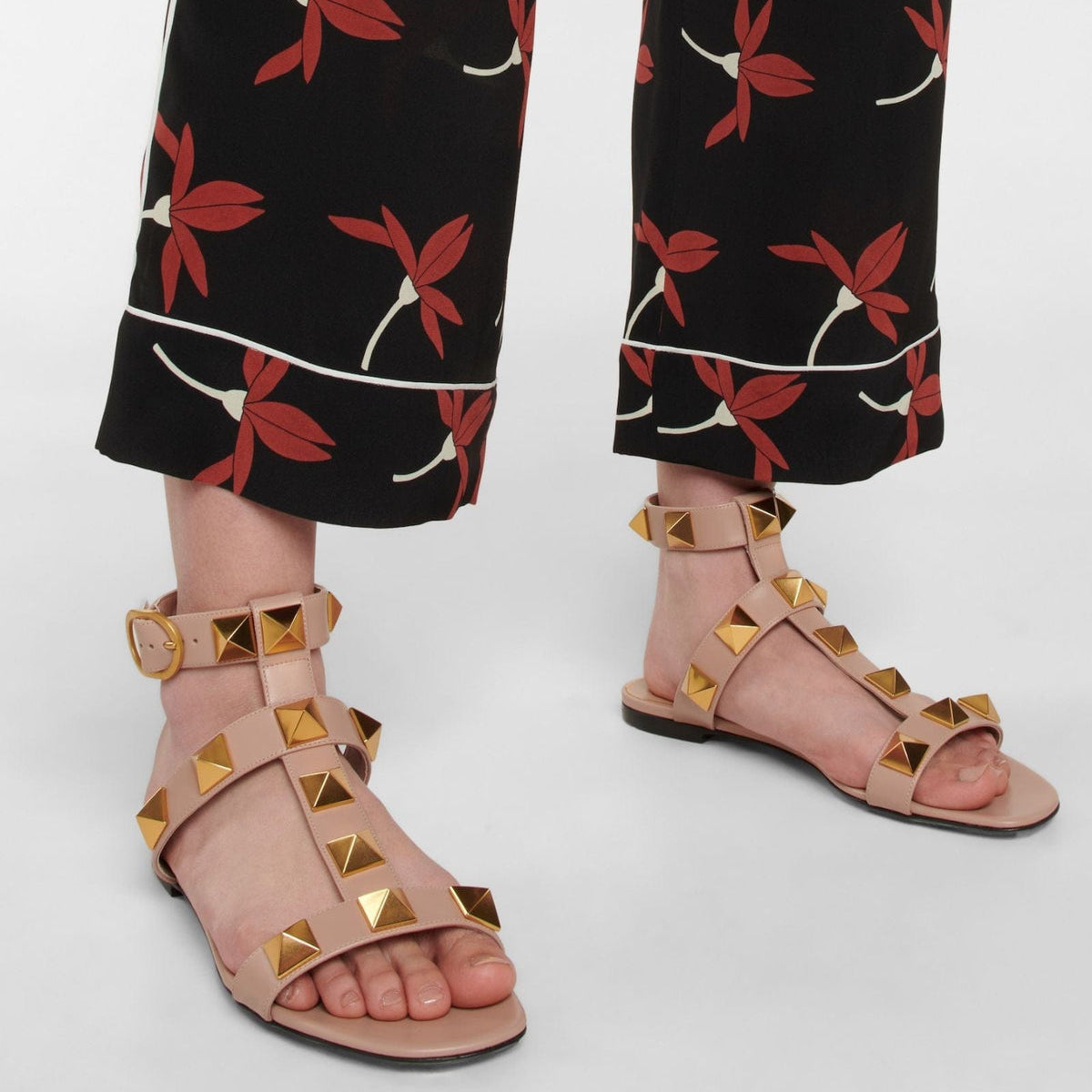 Pink studded sandals worn with black pants featuring red floral patterns on a white background