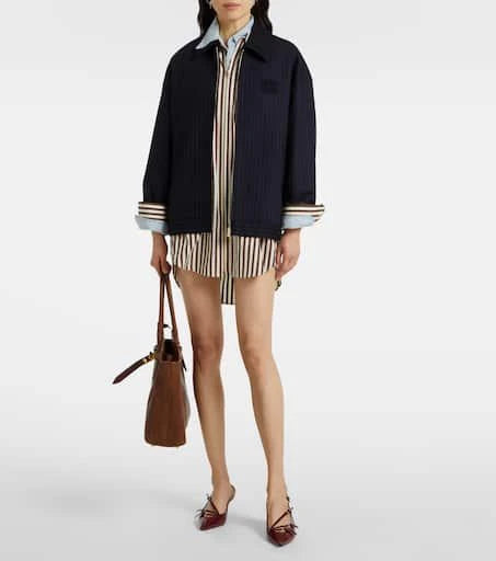 Person wearing a navy coat over a striped shirt with a brown handbag on a white background