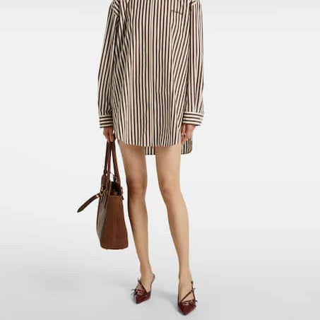 Person wearing a striped shirt dress with a brown handbag on a white background