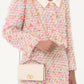 Person wearing a colorful floral dress holding a cream-colored handbag with a brand logo.