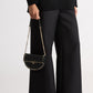 Person wearing black pants and holding a black handbag with studs on a white background