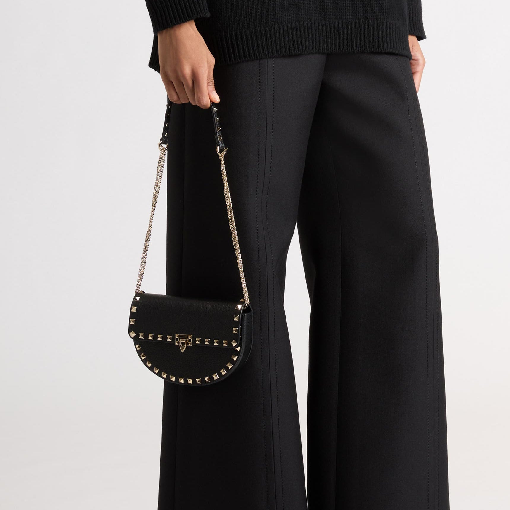 Person wearing black pants and holding a black handbag with studs on a white background