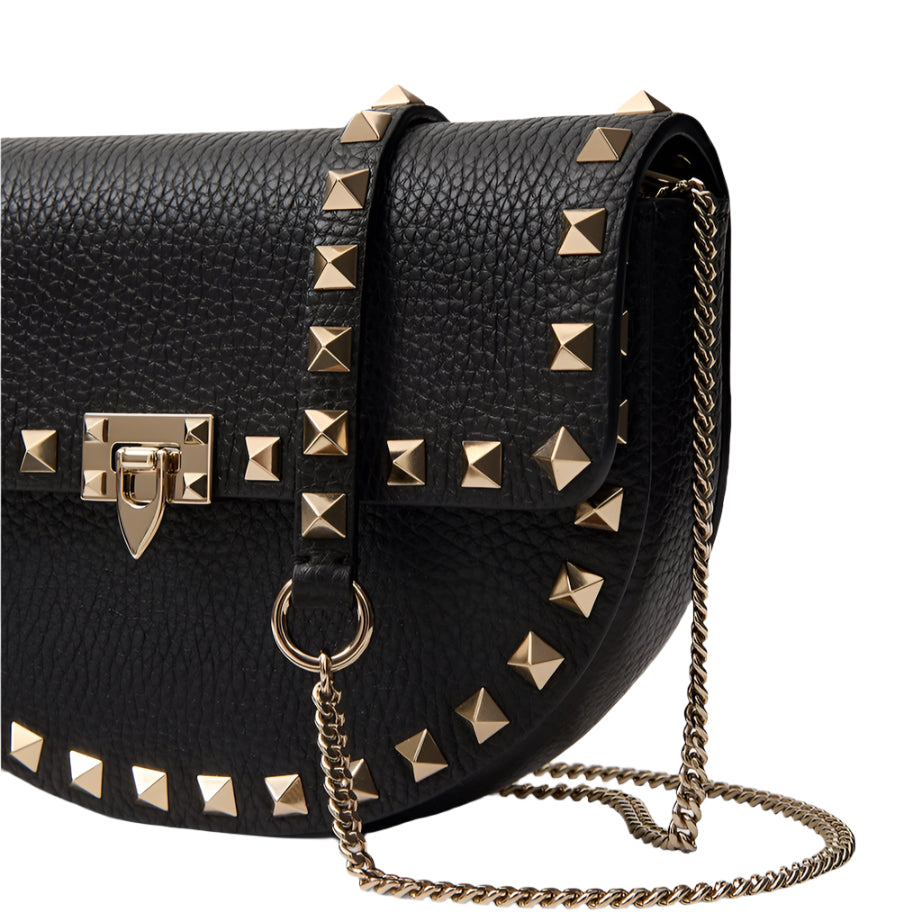 Black leather handbag with gold studs and chain strap on a light gray background