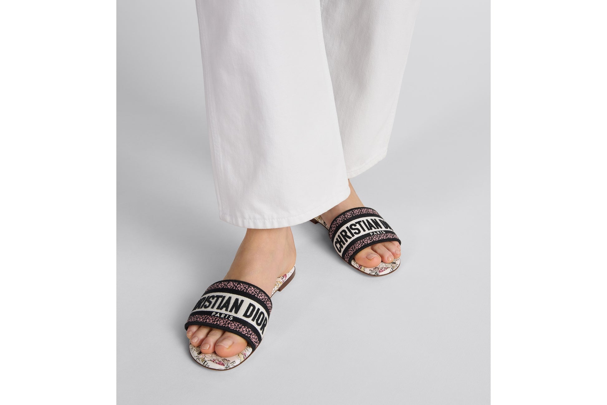 Person wearing black sandals with 'Christian Dior' branding on a light gray background