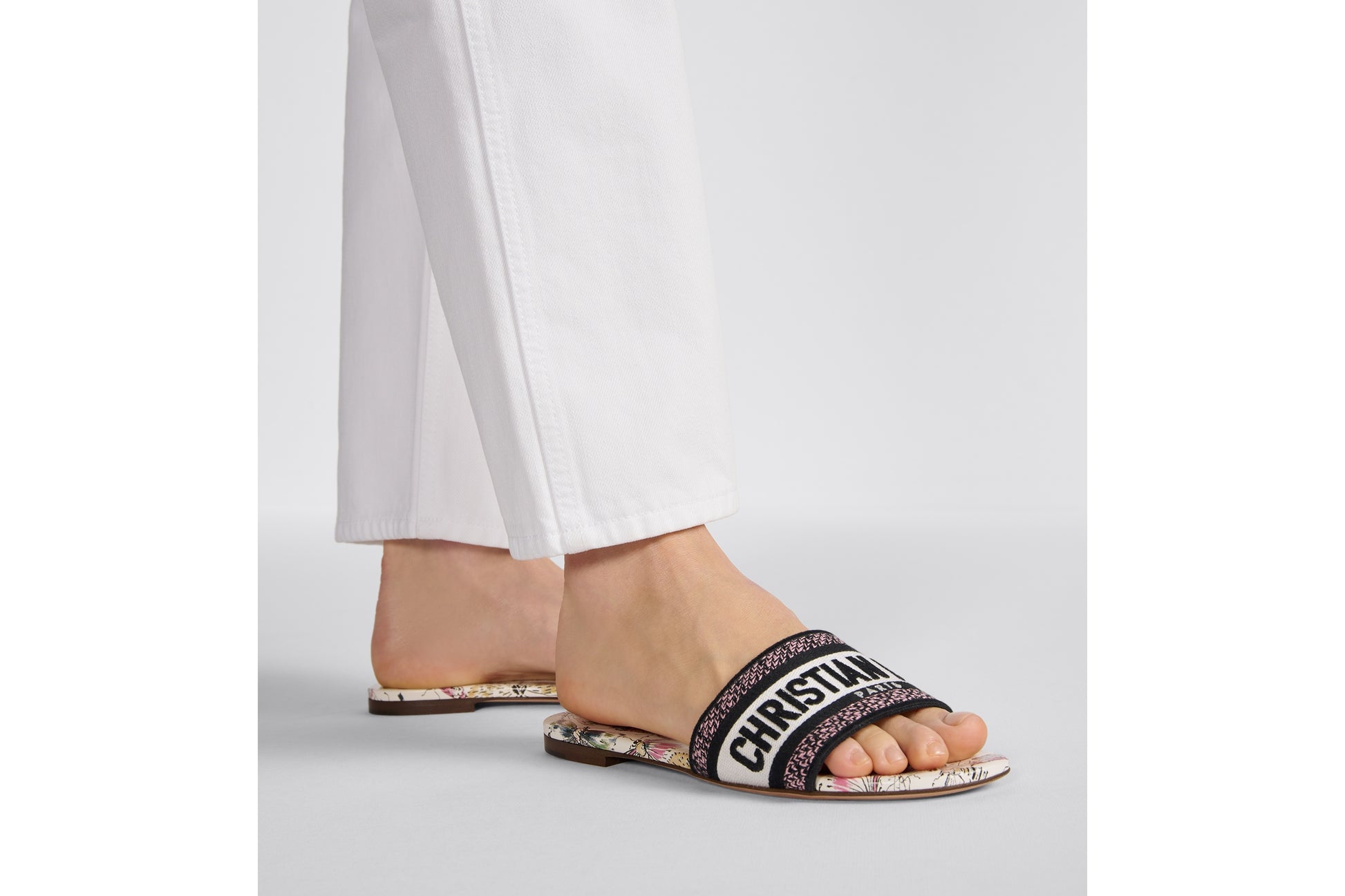 Black slide sandal with 'Christian Dior' logo worn by a person on a light gray background