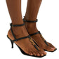 Black high-heeled YSL sandals with black straps worn by a person on a light gray background