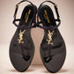 Black sandals with gold logo on a beige background