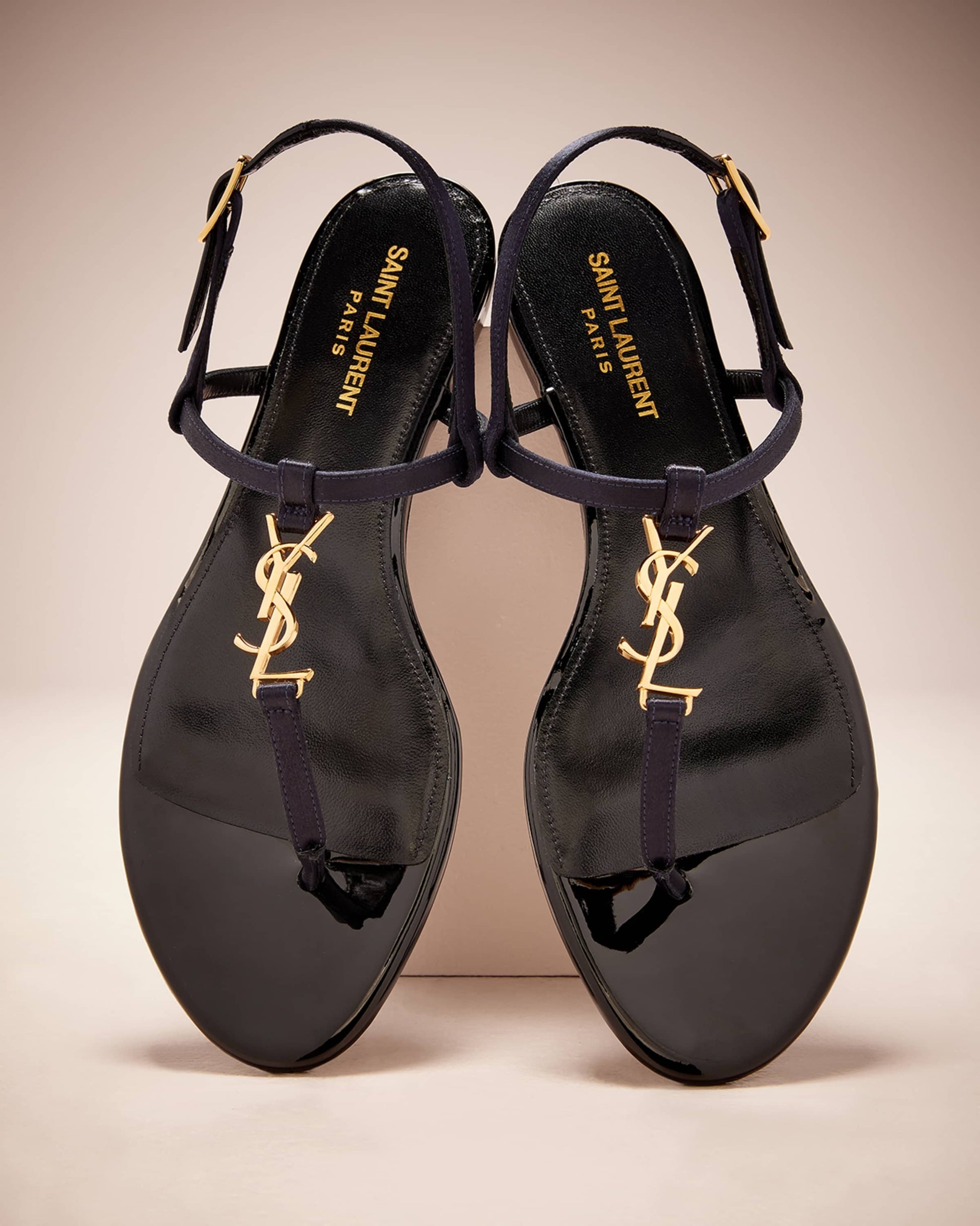 Black sandals with gold logo on a beige background