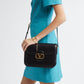 Woman wearing a turquoise dress holding a black handbag with a gold clasp on a white background