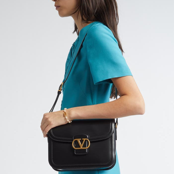 Woman wearing a turquoise dress holding a black handbag with a gold logo.
