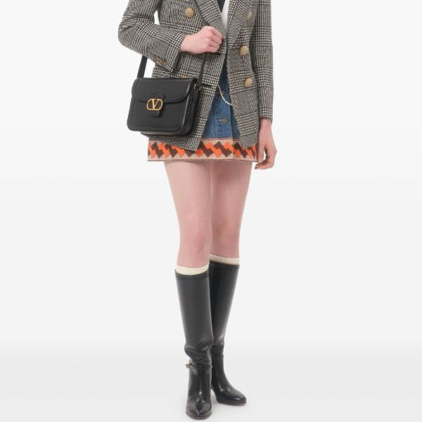 Person wearing a plaid blazer, patterned skirt, and black rain boots on a white background