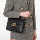 Person wearing a checkered blazer with a black handbag featuring a gold logo.