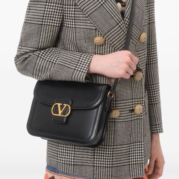 Person wearing a checkered blazer with a black handbag featuring a gold logo.
