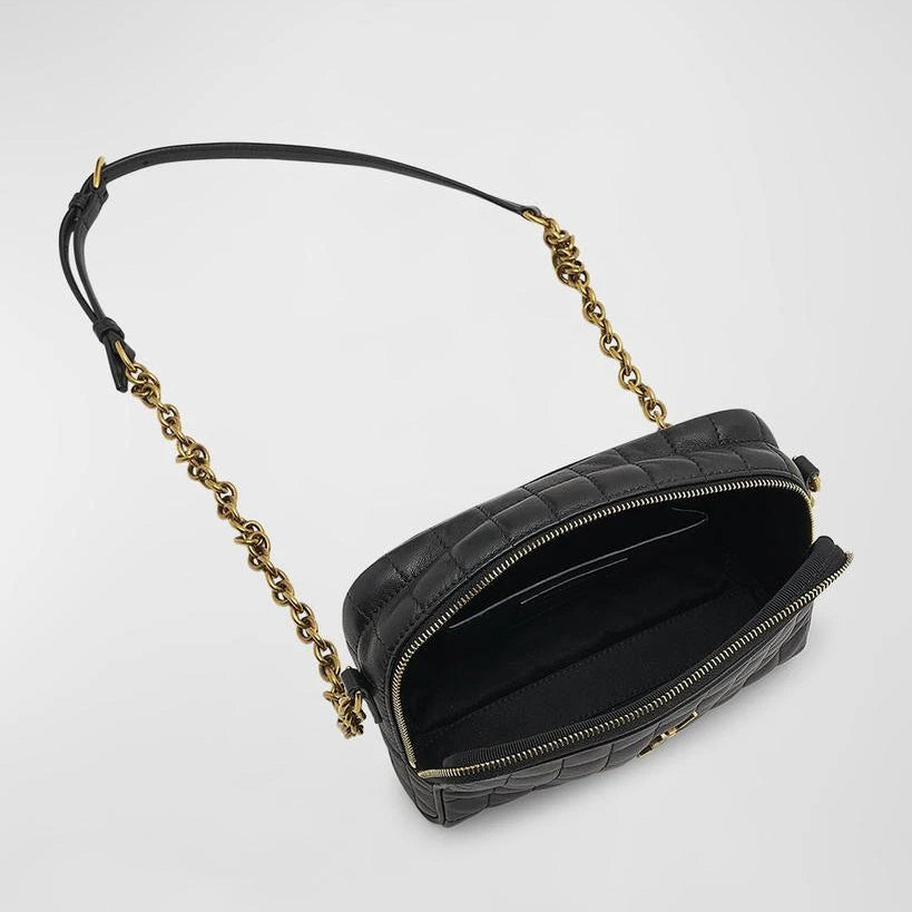 Black quilted handbag with gold chain strap on a light gray background