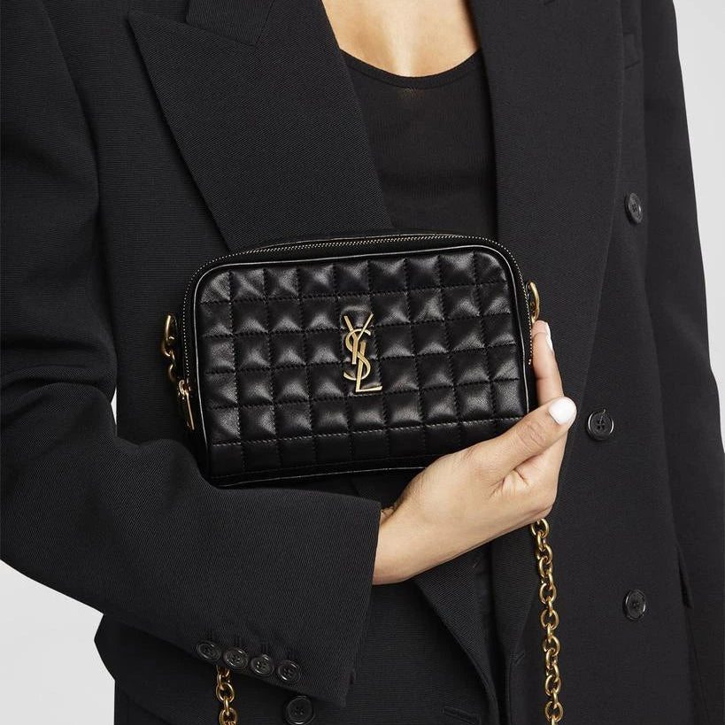 Black quilted handbag with gold chain held by a person wearing a black coat.