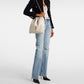Person wearing a black blazer, white top, light blue jeans, and carrying a cream-colored handbag on a white background