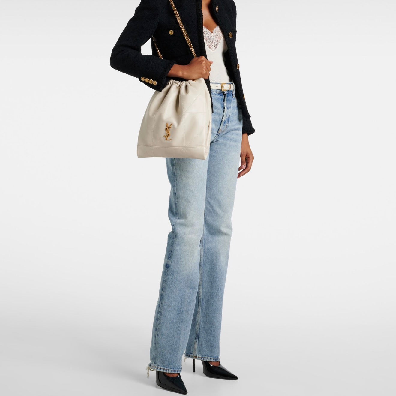 Person wearing a black blazer, white top, light blue jeans, and carrying a cream-colored handbag on a white background