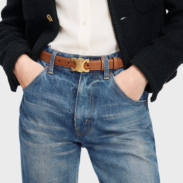 Person wearing blue jeans with a brown belt and black jacket on a light gray background