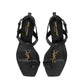 Black high-heeled sandals with gold logo on a white background