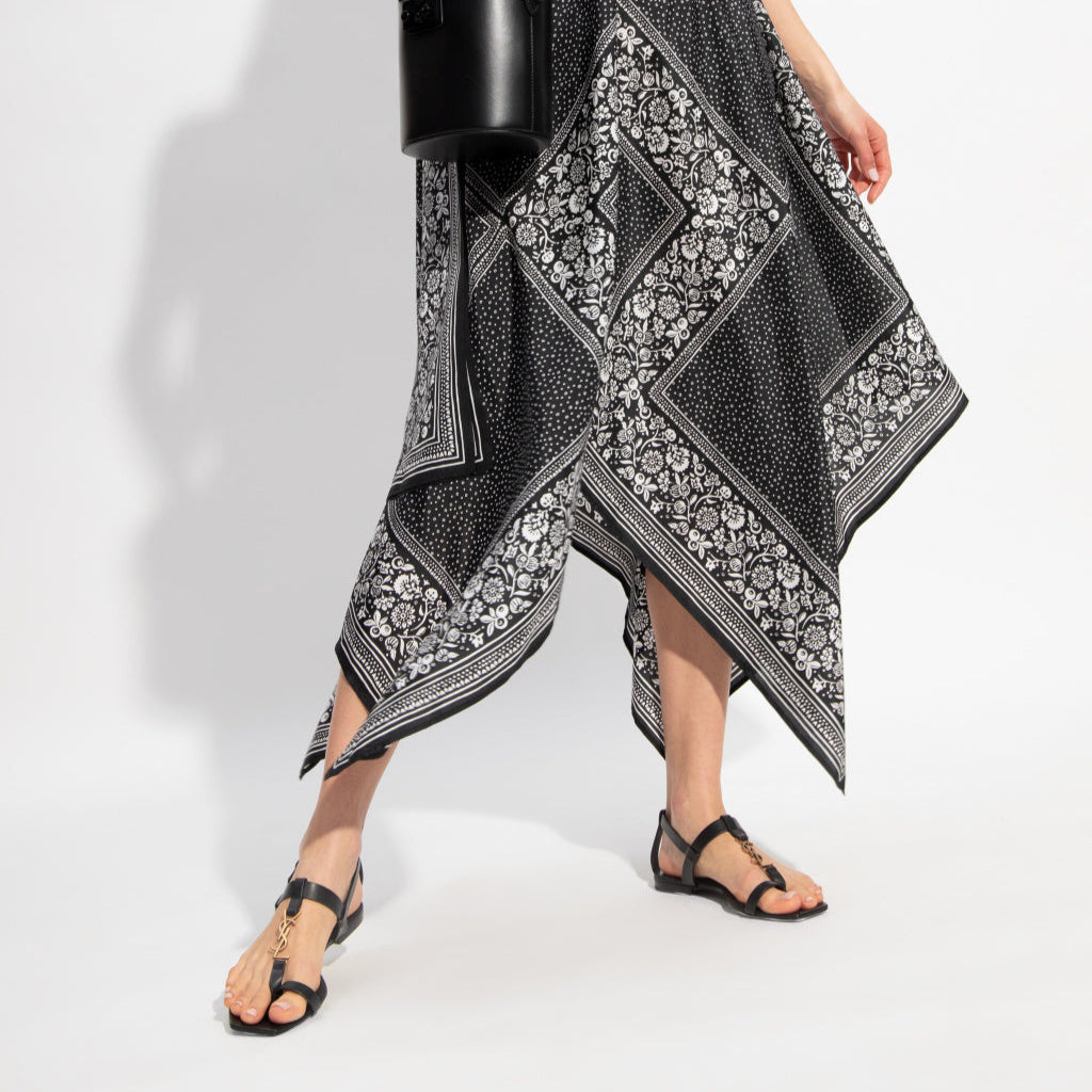 Woman wearing a black and white patterned dress holding a black handbag on a white background