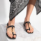 Person wearing black sandals and a black and white patterned scarf on a light gray background