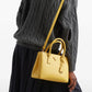 Person wearing a gray cable knit sweater with a yellow handbag on a white background