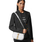 Woman holding a white crossbody bag with a brand logo on a plain background
