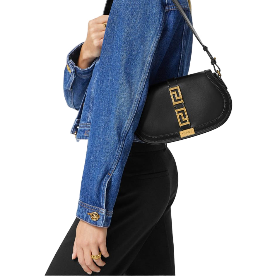 Person wearing a black Versace handbag with a gold emblem on a plain background